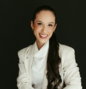 Smiling woman in white blazer sitting in a chair.